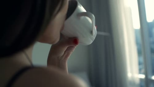 Woman Drinking Coffee by Window in City Apartment