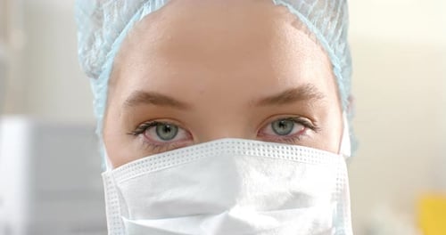 Porträt einer kaukasischen Chirurgin mit OP-Kappe und Gesichtsmaske, Zeitlupe