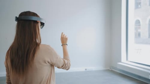 Junge Hipster-Frau mit holographischer Augmented-Reality-Brille, die im leeren Büro steht und es kartografiert.
S
