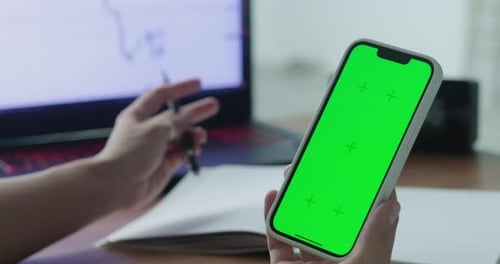 A Woman's Hand Phone with Green Mockup Screen Chroma Key Holds a Smartphone of the Workspace