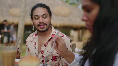 LGBTQ Man Dines with Friends at Beachside Cafe Enjoying Meal Group Relaxes By Ocean Shares Laughter