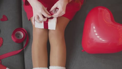 Woman Tying Ribbon on Gift with Heart Balloon