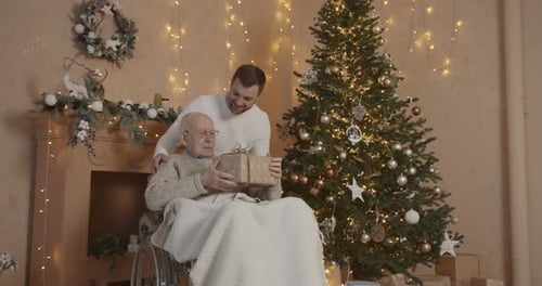 Young Man Giving Christmas Gift to Senior in Wheelchair