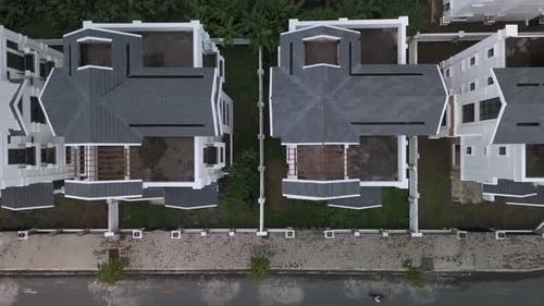 A newly constructed row of identical large white multi story villa styled houses along a road.