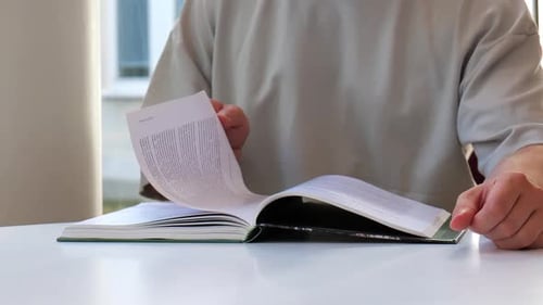 Mann blättert langsam die Seiten eines Buches um. Auf einem Tisch sitzen und beim Lesen lernen.