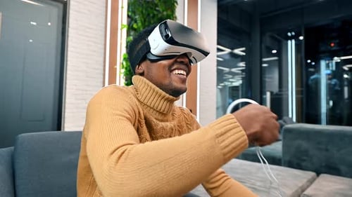 A black man exploring virtual reality using VR glasses and controllers in an office
