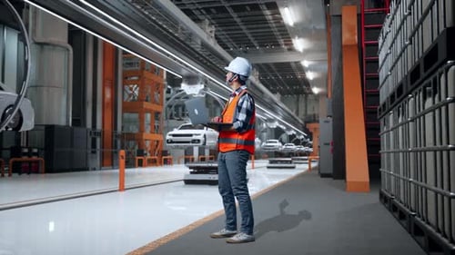 Vue latérale complète du corps d'un ingénieur asiatique travaillant sur un ordinateur portable dans une usine de voitures électriques