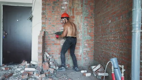 Un constructor retira una pared de ladrillos con una herramienta eléctrica durante la renovación interior