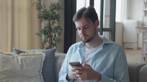 Man Using Smartphone on Couch Indoors Daytime
