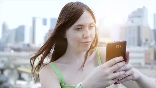 Woman Using Phone On Rooftop Overlooking City