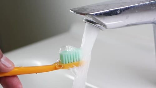 Slow Motion of Holding Toothbrush Under Flowing Water in Bathroom Closeup