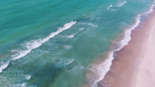 Toma aérea de alta altura de un Zumbido sobre las olas que rompen en una playa de arena rosada que se mueve hacia el mar