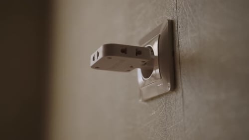 Foto recortada em closeup de uma pessoa inserindo o adaptador de vários soquetes e o cabo de alimentação na tomada de parede
