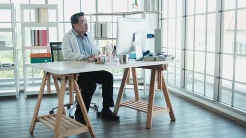 Professional Asian doctor focuses on work, using computer in hospital office.