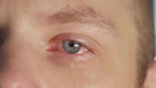 Tear slowly falls from caucasian man's eye, close up handheld