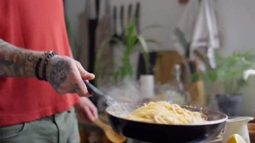 Cropped shot of unrecognizable man tossing hot spaghetti in skillet while cooking pasta in kitchen