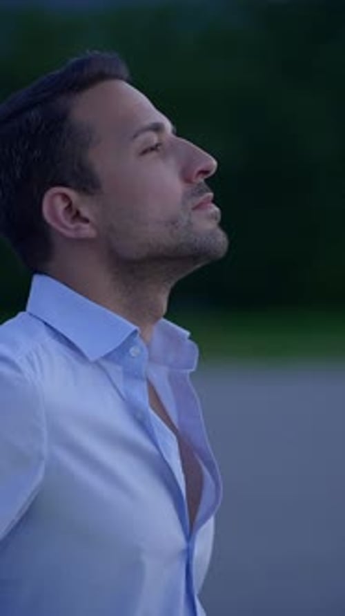 Pensive Man in Blue Shirt Leans on Car