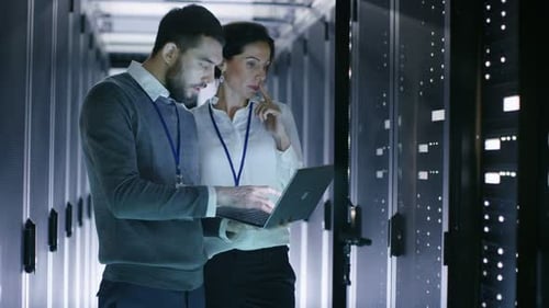 Male and Female Server Engineers Work on a Laptop in Data Center. He Opens Rack Server Cabinet.
