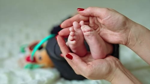 Careful loving mommy’s hands hold tiny baby feet. Little child moves his cute toes. Close up.