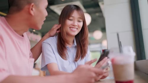 Close-up of two young male and female friends talking and looking at smartphones in a coffee and bur