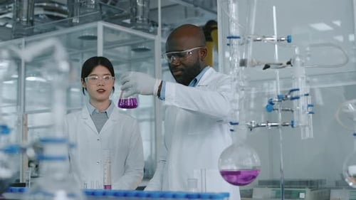 Multiethnic Researchers Discussing Purple Chemical Liquid in Flask in Laboratory