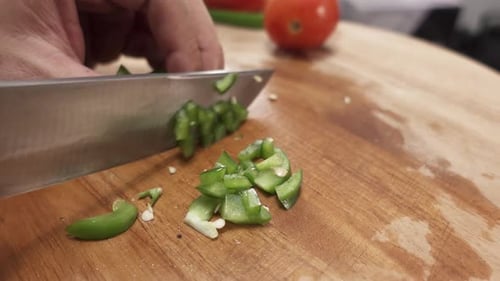 Close-up of a hand chopping green bell pepper into small pieces with a kitchen knife