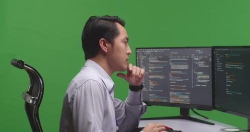 Asian Man Developer Thinking While Write Code With Multiple Computer Screens In Green Screen