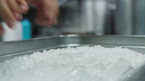 Close up view of a chef collecting ice from a aluminum tray in a kitchen of a French chef restaurant
