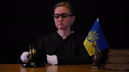 Female Judge in Dark Robe Hitting a Gavel Next to the Ukrainian Flag and Law Books