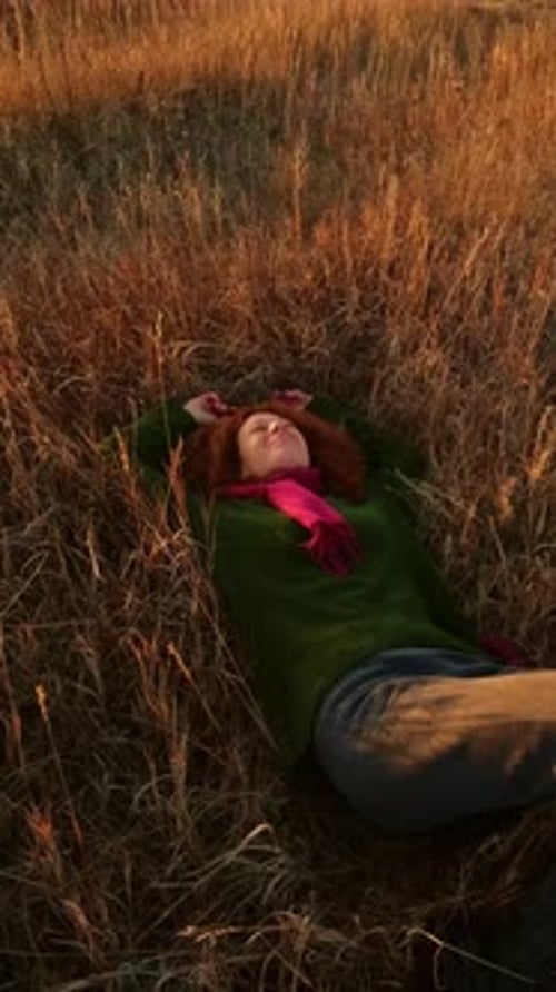 Femme allongée dans un champ d'herbe dorée souriant joyeusement avec une écharpe vibrante et une lumière chaude