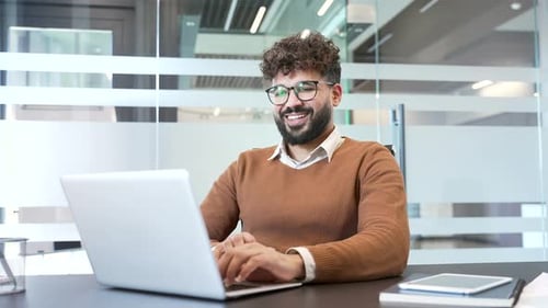 Smiling Man Working on Laptop in Modern Office