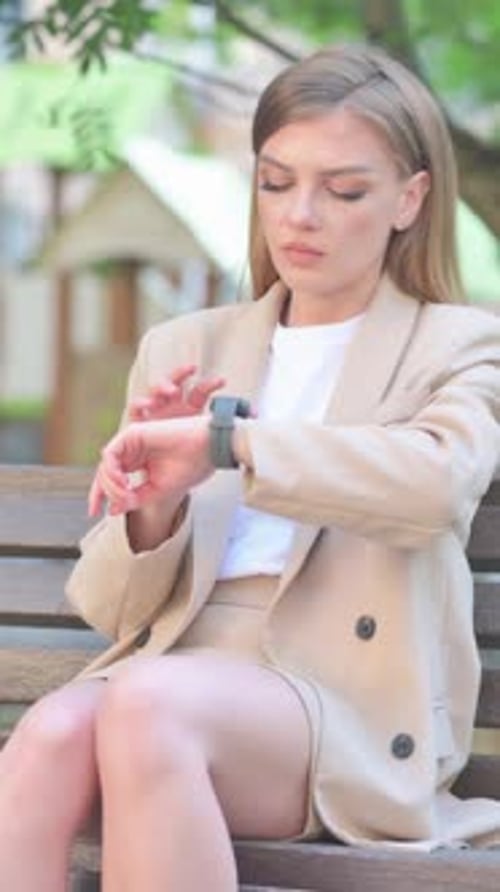 Woman in Suit Sitting and Checking Smartwatch Outside