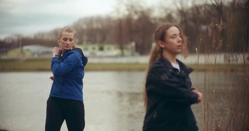 Female Athletes Doing Warm Up Exercise Against Lake
