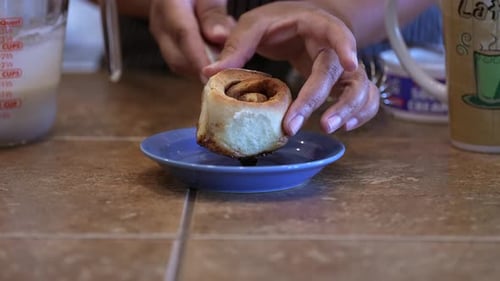Placing a fresh baked cinnamon roll on a plate for icing and serving - side view in slow motion