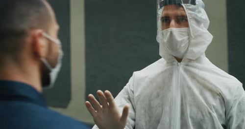 A man is getting temperature measured with infrared thermometer gun by medical staff with PPE suit