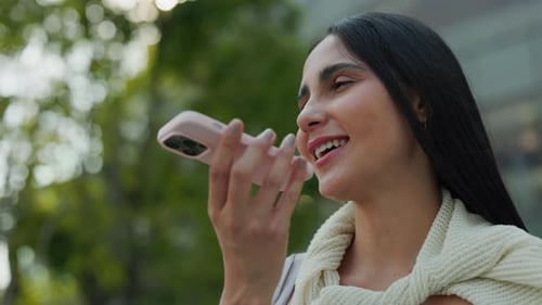 Portrait of Cheerful Brazilian Woman Records Audio Message on Smartphone in Park