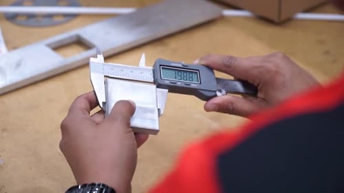 Female manufacturing engineer using caliper to measure material, hands close up
