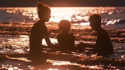 Siblings Bonding At The Beach As Glinting Sea Waves Approach