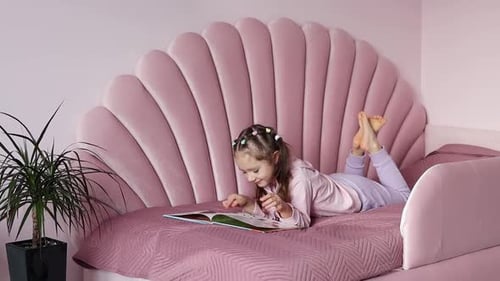 A little girl is lying on the bed looking at the book in slow motion