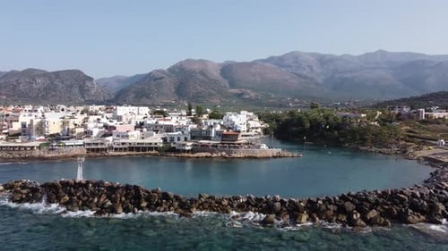 Drone flies high towards the city of Sissi on Crete Greece - you can see the city and the harbor in