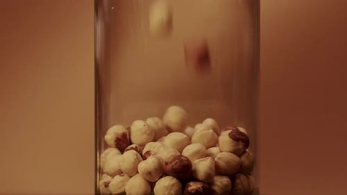 Hazelnuts Pouring into Glass Jar Filling to Brim