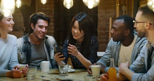 Slow motion of smiling friends having coffee at cafe and having fun with mobile cell phone. Shot i