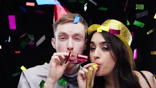 4k video footage of two people blowing party horns against a studio background
