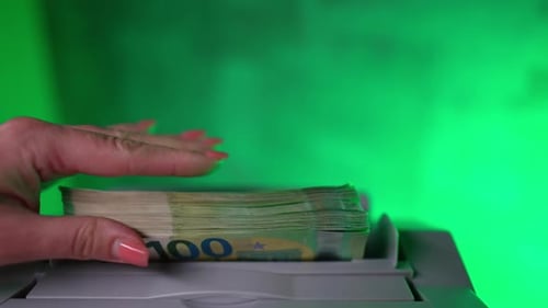 Hand puts a pile of green euro hundred banknotes to a money counting machine.