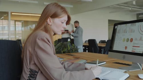 Businesswoman Working with Financial Data and Taking Notes at Office Desk