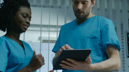 In the Hospital Male and Female Nurses Use Tablet Computer while Talking. Professional Medical Staf
