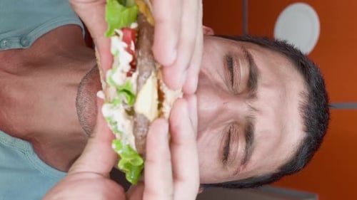 Man Eats Big Meat Burger with Pleasure in Restaurant Guy Casually Eats Fast Food