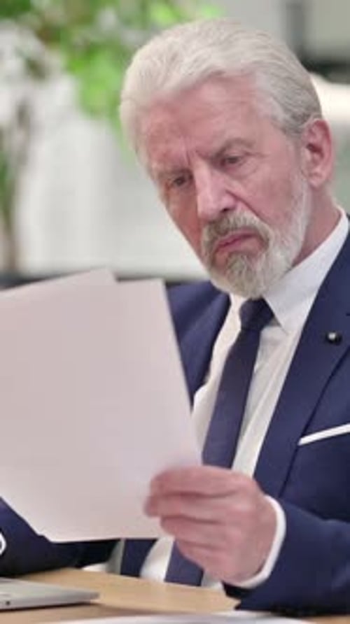Senior Businessman Analyzing Documents at Desk