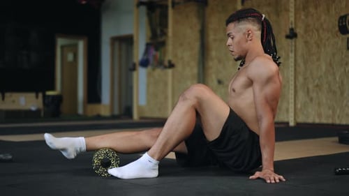 Athletic Man Foam Rolling Lower Leg in Gym