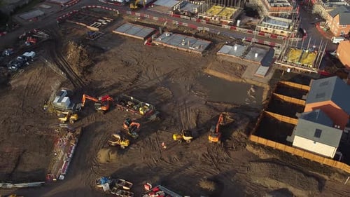 Town housing development aerial view circling above muddy property foundation construction site